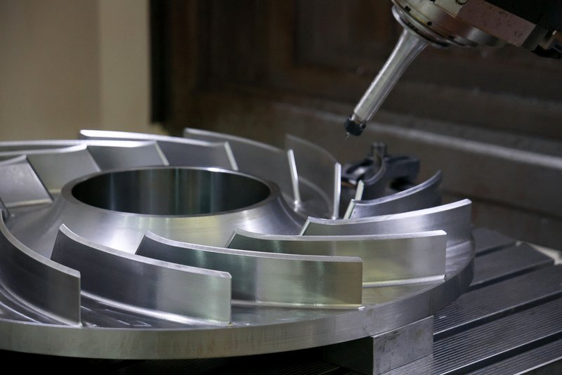 Идёт фрезерная обработка диска с лопатками колеса рабочего нагнетателя Ц-16 на пятикоординатном станке DMU 120. Станок, обладающий пяти осями может одновременно перемещать исполнительные звенья станков по всем пяти осям. Это позволяет проводить более сложные операции, такие как контурная фрезеровка, где инструмент должен двигаться по криволинейным поверхностям сложной детали под различными углами.